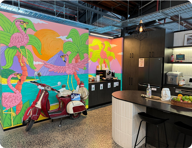 Colorful mural featuring flamingos and tropical scenery in a modern office kitchen with a vintage scooter, emphasizing a vibrant workspace atmosphere at Perceptiv Media.
