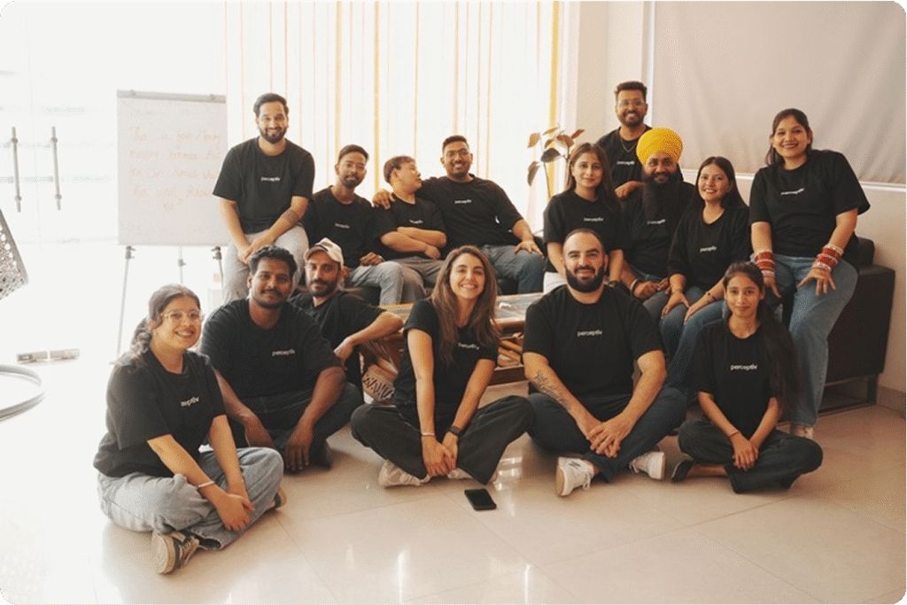 Team of Perceptiv Media members in black t-shirts, seated together in a bright office space, showcasing collaboration and creativity in their work environment.