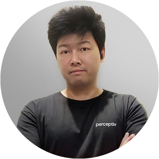 Graphic designer Johan Fu from Perceptiv Media, wearing a branded shirt, posing with arms crossed against a neutral background.