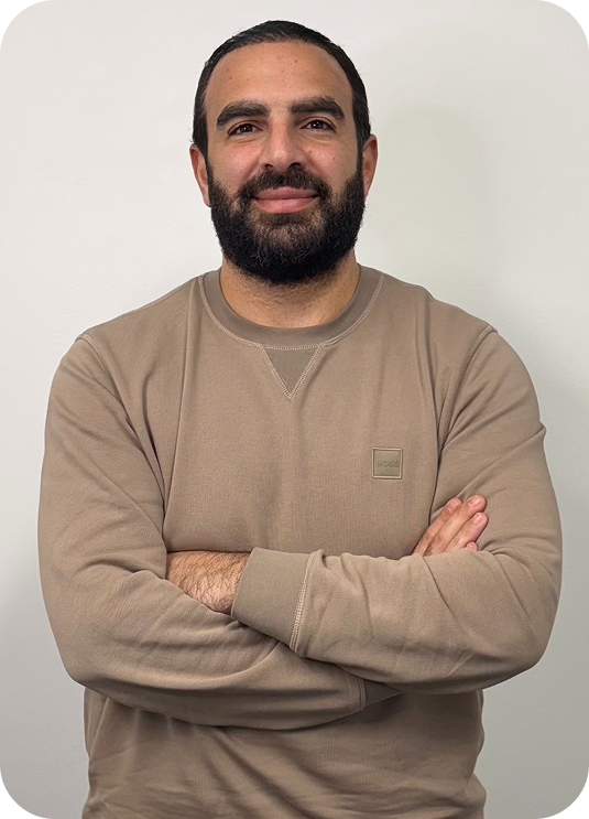 Nicholas Adamou, Sales & Operations lead at Perceptiv Media, smiling with arms crossed, wearing a beige sweatshirt against a neutral background.