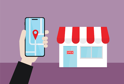 Hand holding smartphone displaying a map with location pin, next to a small shop with a red and white striped awning and an "OPEN" sign, symbolizing local SEO strategies for business visibility.