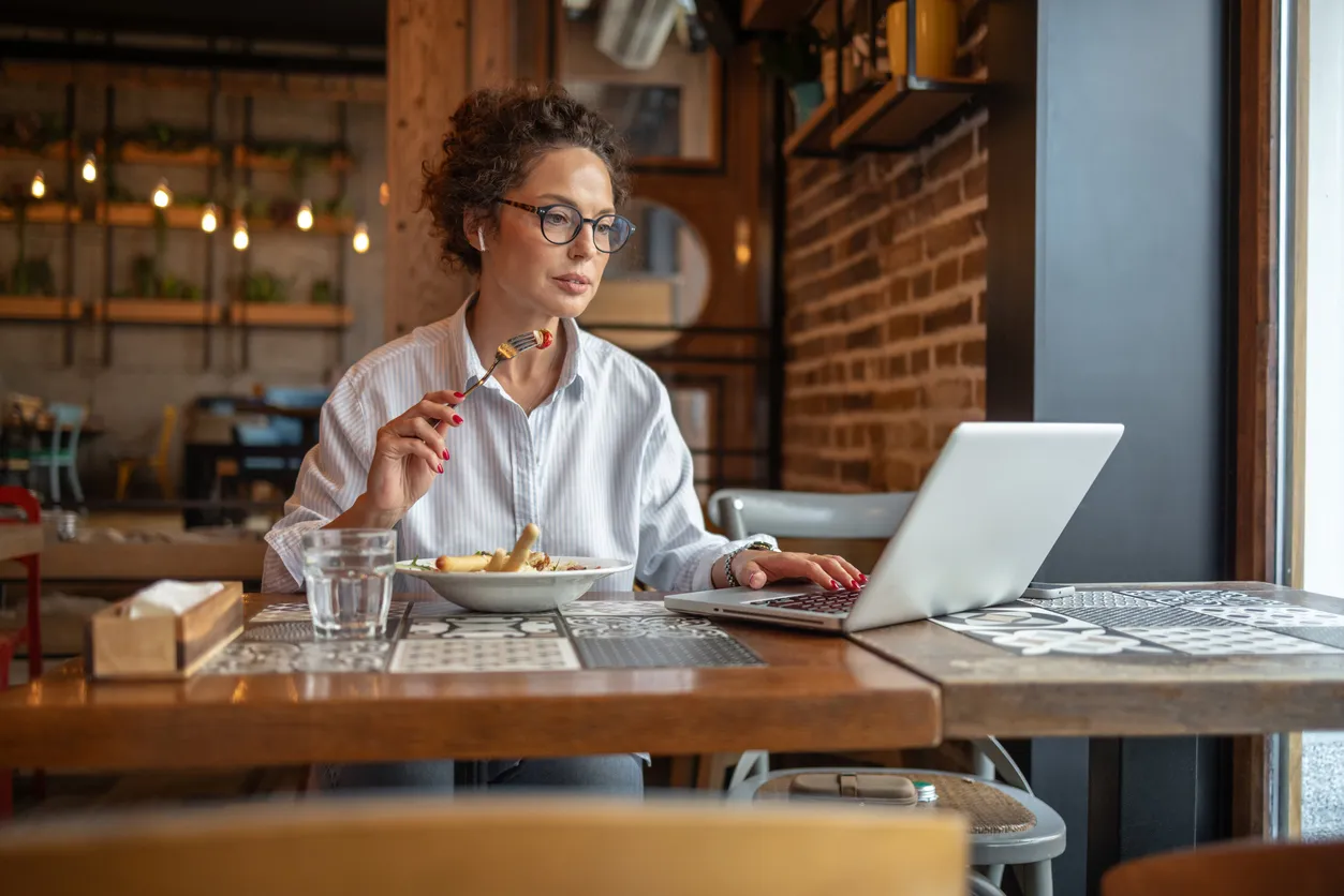 Woman eating lunch while working on a laptop in a cozy café setting, illustrating the blend of productivity and dining for small business owners seeking effective SEO strategies.
